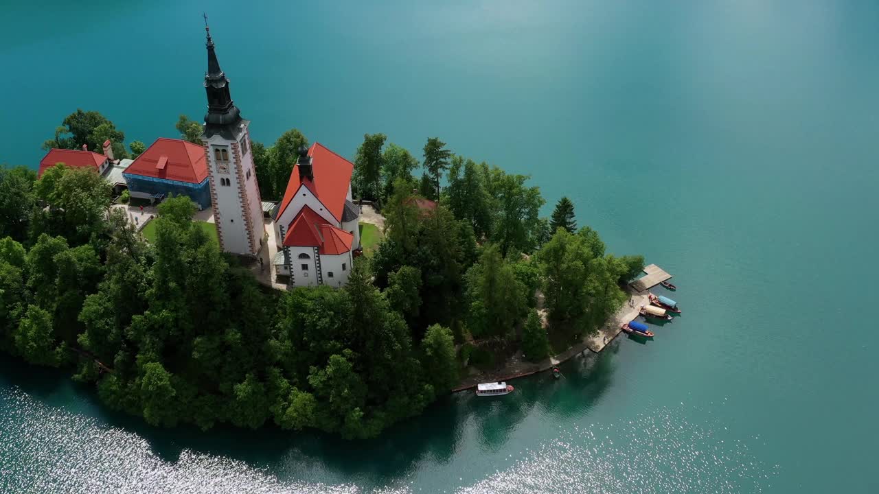 空中:倾斜拍摄的教堂在树上在岛上，无人机在阳光下飞过湖泊-流血，斯洛文尼亚视频下载