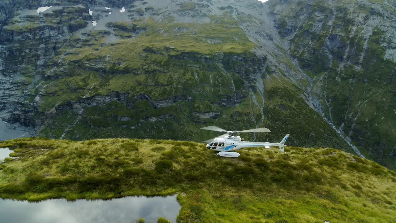 航拍:旋转旋翼叶片的直升机在山顶，无人机飞过绿色植物-奥克兰，新西兰视频素材