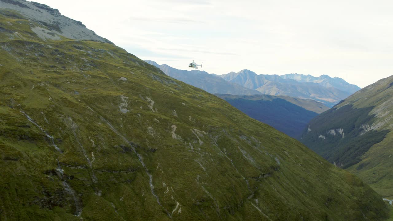 航拍:拍摄直升机在绿色山上飞行的风景-奥克兰，新西兰视频素材
