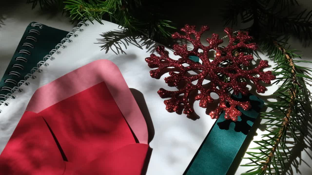 圣诞静物与圣诞树的树枝，记事本和一个红色的信封。交叉的阴影线。圣诞组成。视频素材