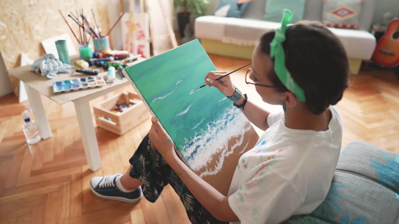 年轻的女画家坐在家里的地板上在画布上作画视频素材