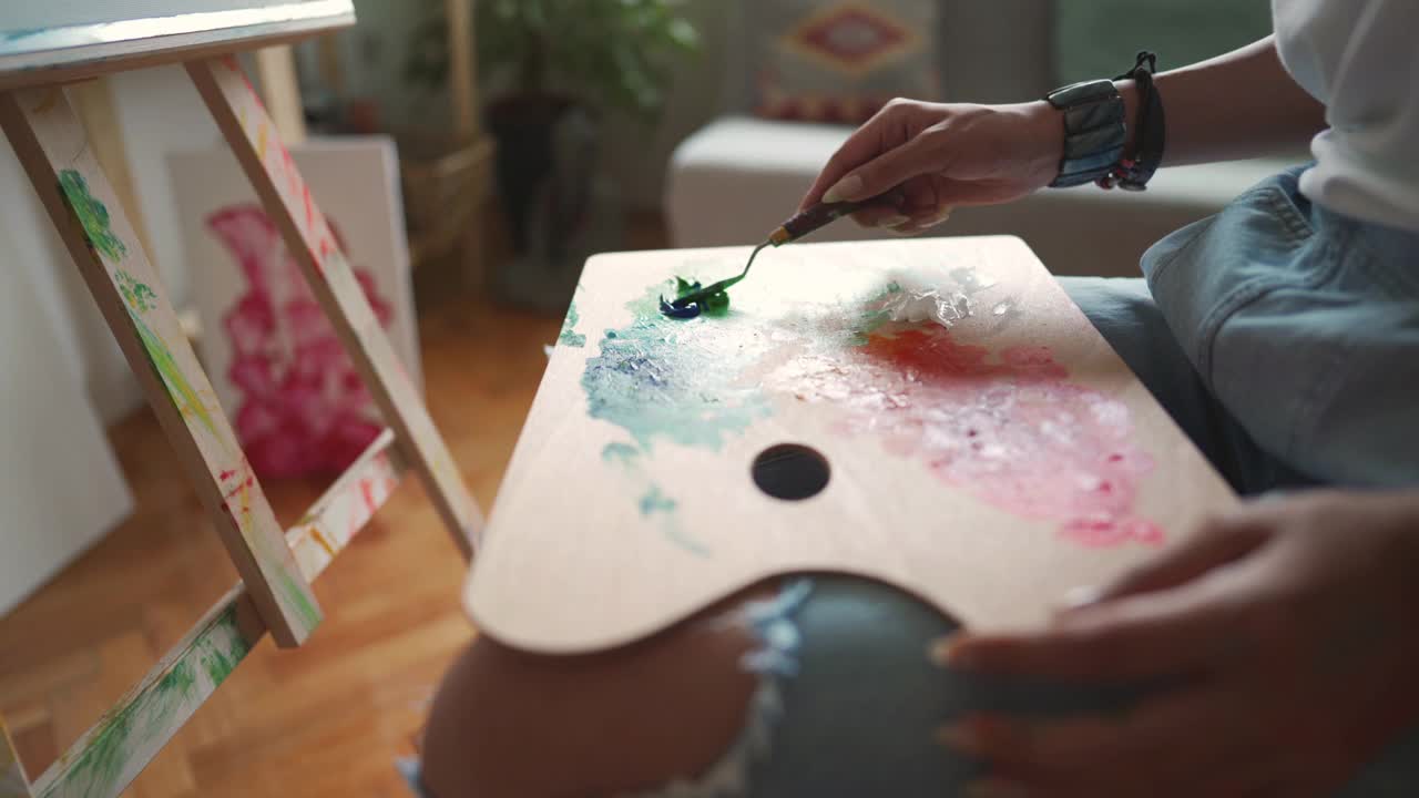 一个不知名的女艺术家用抹刀在调色板上混合油/丙烯酸颜料的b卷视频下载