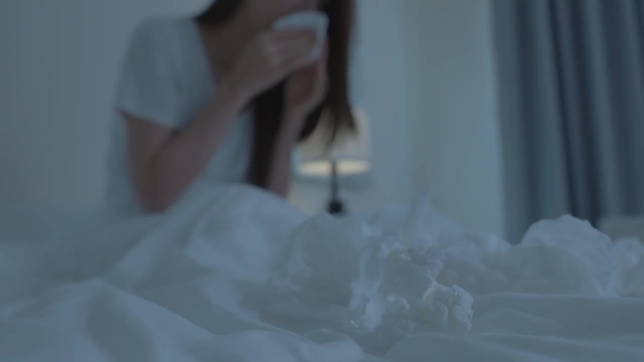 亚洲生病的女孩穿着睡衣醒来在床上打喷嚏。有魅力的年轻女子感觉不舒服，并且患有过敏症，睡觉时用纸巾捂住鼻子。视频素材