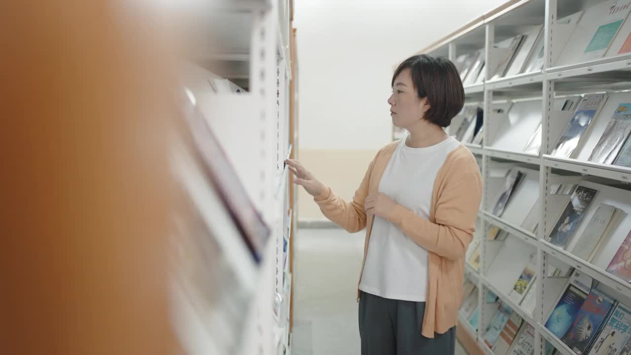 亚洲女人在图书馆的书架上看杂志视频购买
