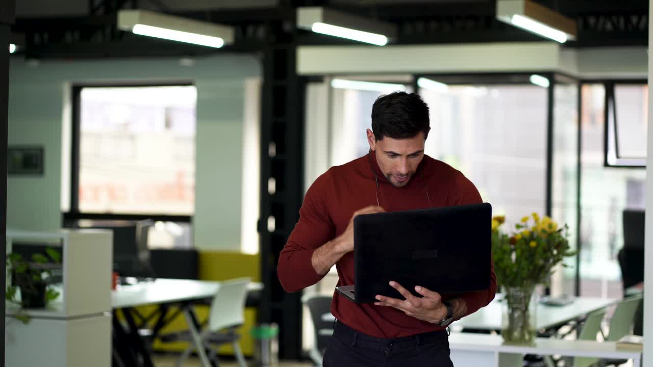 一个拉丁裔男子在他工作的办公室里摆弄着笔记本电脑视频素材