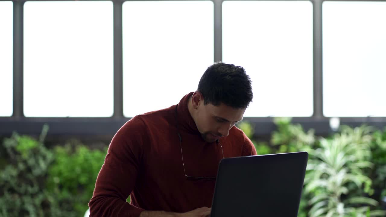 一个拉丁裔男子在他工作的办公室里摆弄着笔记本电脑视频素材