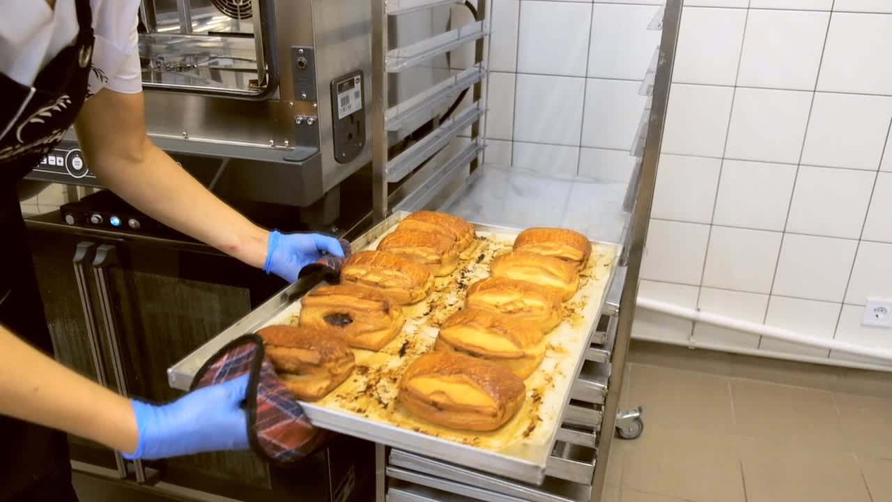 一位女面包师把热面包从烤箱里拿出来。视频下载