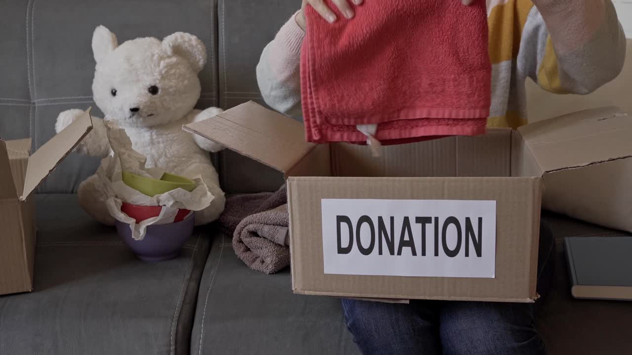 她膝盖上放着一个打开的慈善盒子，一个女人正在里面放东西视频素材
