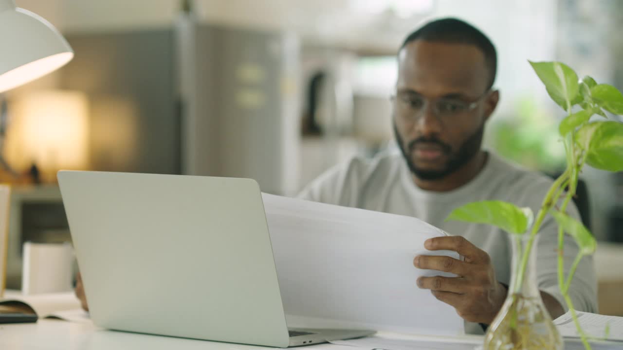 快乐的非洲裔年轻人在家里用笔记本电脑工作，早上坐在家里办公室的办公桌前喝咖啡。在家工作的概念。视频下载