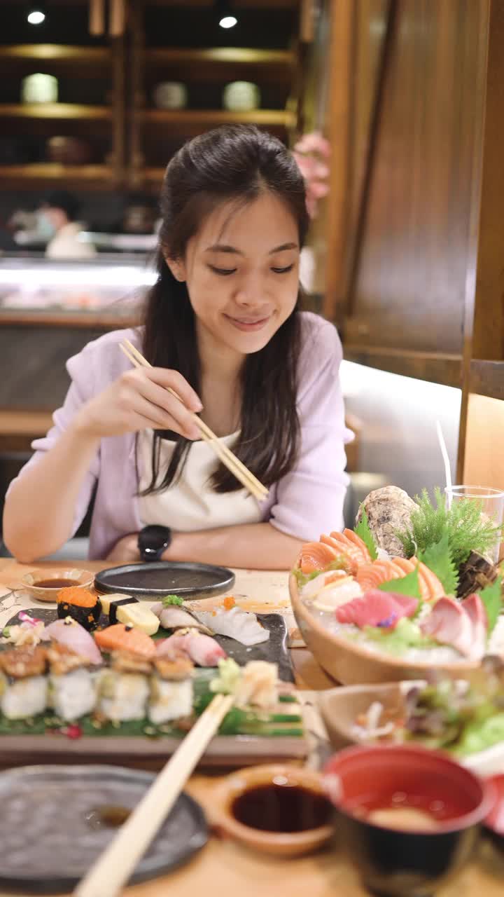 Z一代年轻的亚洲女性享受着豪华的日本料理与什锦寿司，海鲜，牡蛎，生鱼片在餐厅的餐桌上新鲜供应。亚洲美食和食物。外出就餐的生活方式视频下载