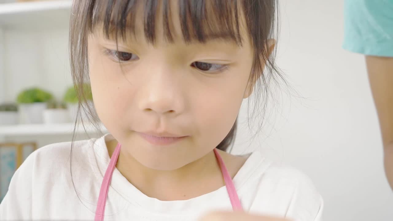 快乐的亚洲孩子在家里学习做饼干，女孩往搅拌碗里撒面粉，慢动作。视频素材