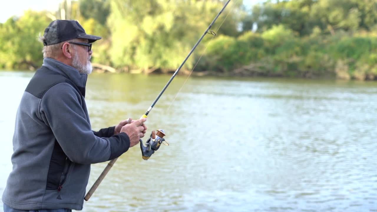 成熟的灰胡子男人，戴着眼镜，渔夫拿着杆，旋转或勺子诱饵，在美好的夏日钓鱼。男人的爱好视频素材