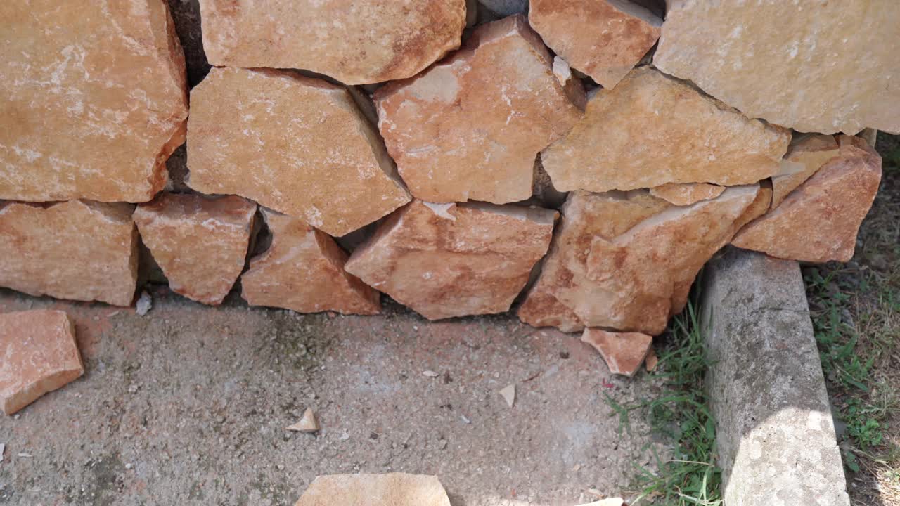 施工现场砌筑石墙的艰苦工作，装饰墙面的橙色砖石，用水泥溶液和不同的工作工具砌筑石材的过程。砖砌建筑视频素材