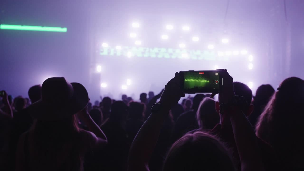 在音乐节上欢呼的人群。专注于跳舞的人用智能手机录音视频素材