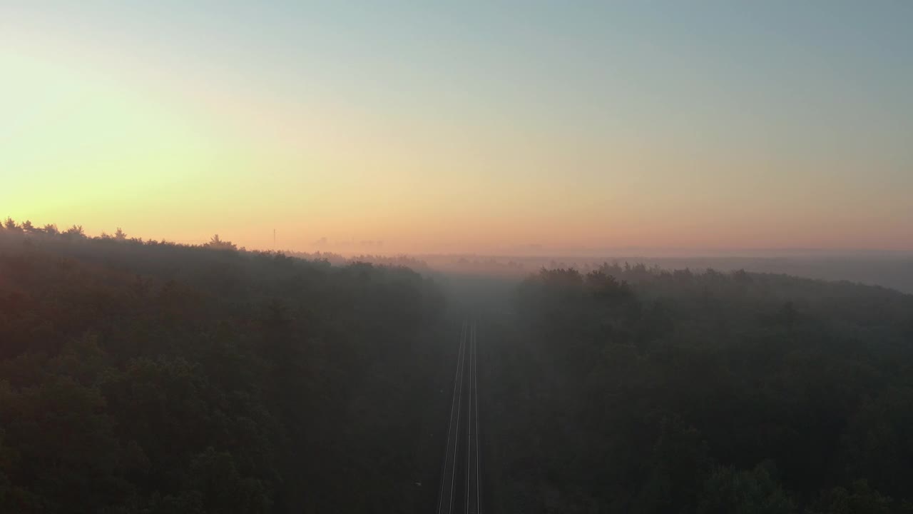 鸟瞰图一个雾蒙蒙的秋天森林与铁路在日出。视频下载