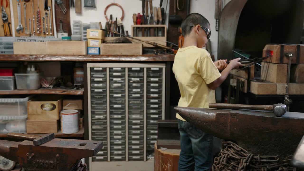 (中景)一个男孩在一家小作坊里练习打铁视频下载