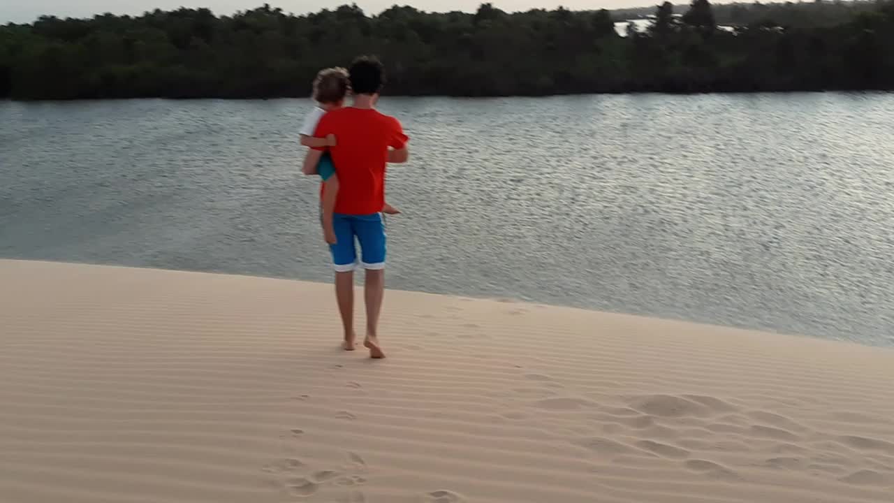 父亲抱着儿子在海边的沙丘上下山视频下载