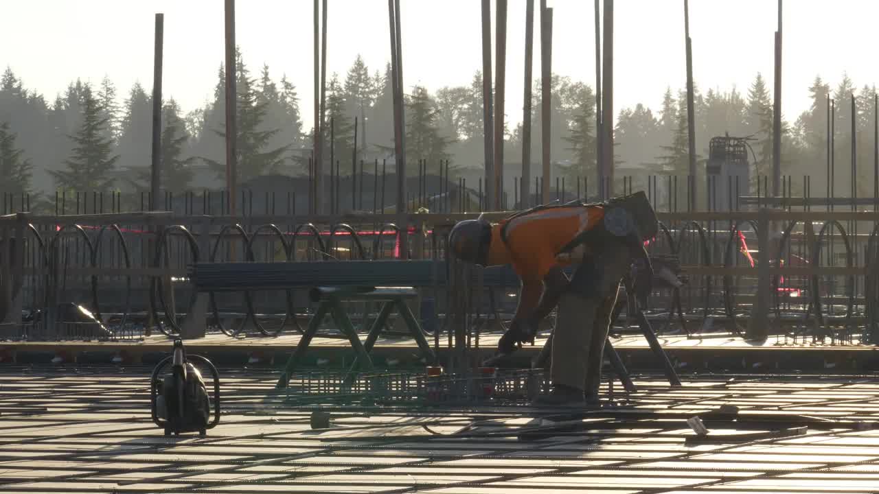 在一个大型商业工地，在混凝土浇筑前，建筑工人将铁丝与钢筋连接起来。视频素材