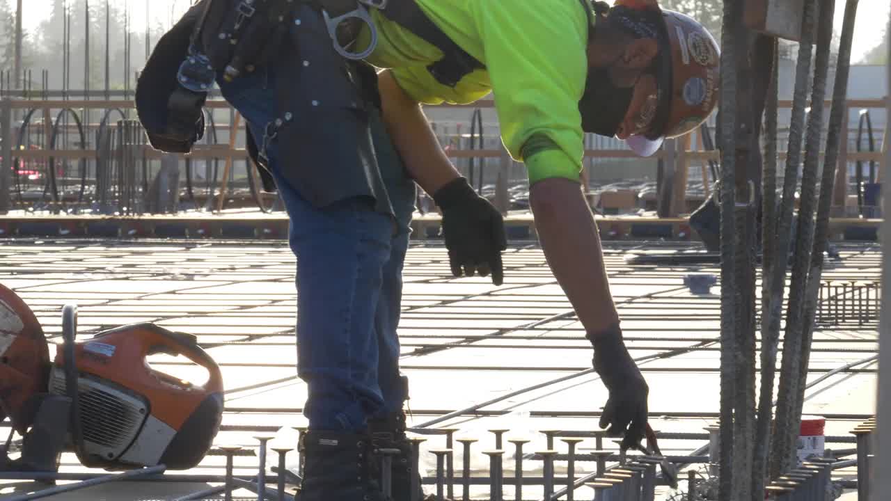 在一个大型商业工地，建筑工人在混凝土浇筑前将电线重新连接到钢筋上。视频素材