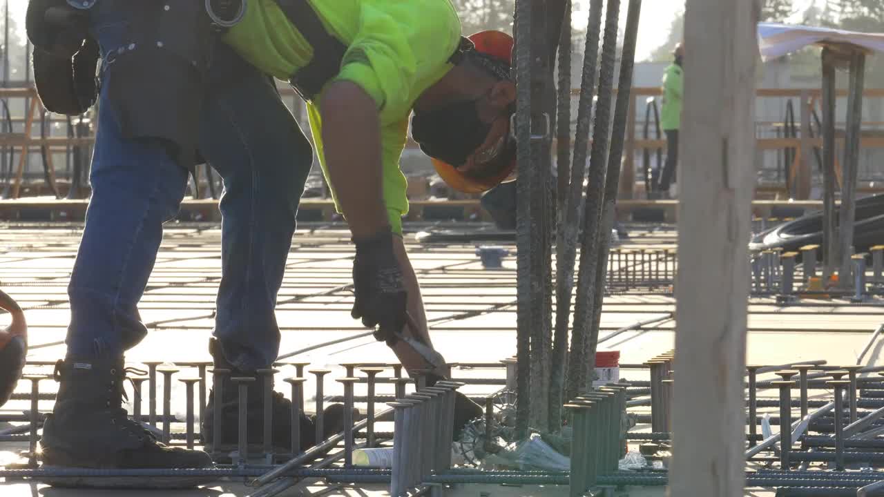 在一个大型商业工地，建筑工人在混凝土浇筑前把铁丝换成钢筋。视频素材