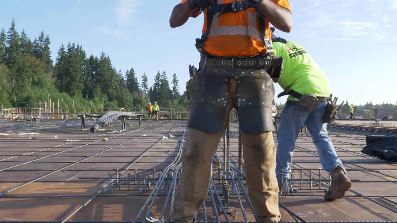 在一个大型商业工地，在混凝土浇筑前，建筑工人将铁丝与钢筋连接起来。视频素材