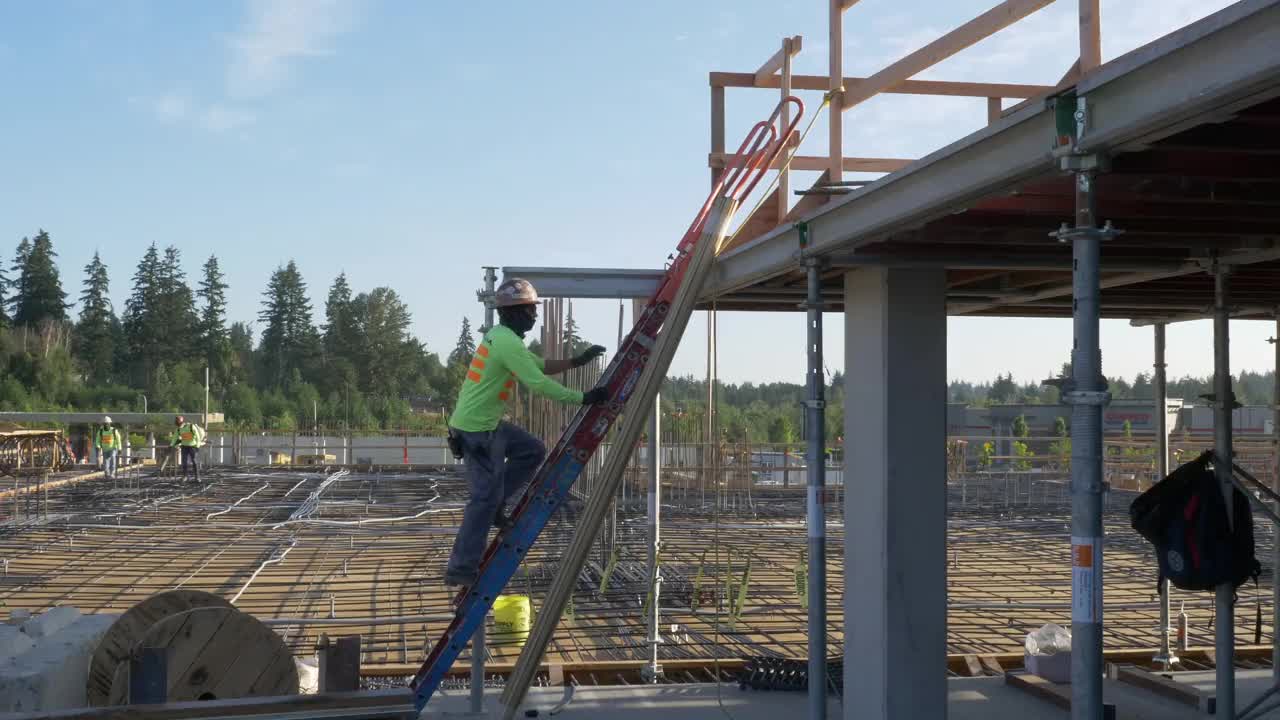 建筑工人在一个大型商业工地上爬梯子。视频素材