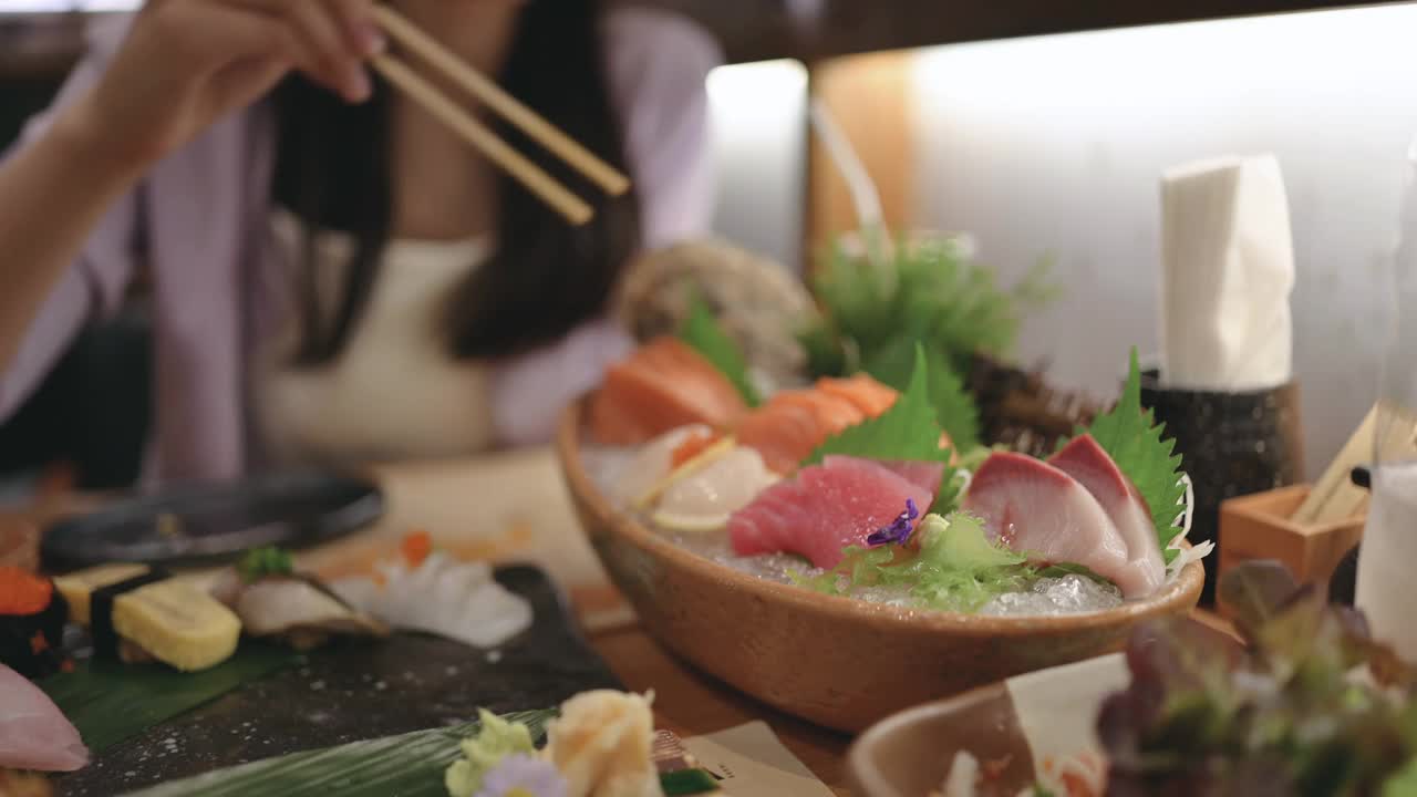 朋友在日本餐厅用餐，餐厅的餐桌上摆满了各式各样的寿司、海鲜、牡蛎、生鱼片。视频素材
