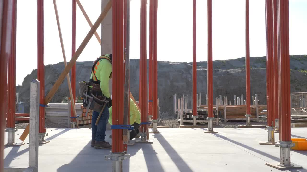 两名建筑工人在一个大型商业工地调整框架和脚手架——摄像机向右平移。视频下载