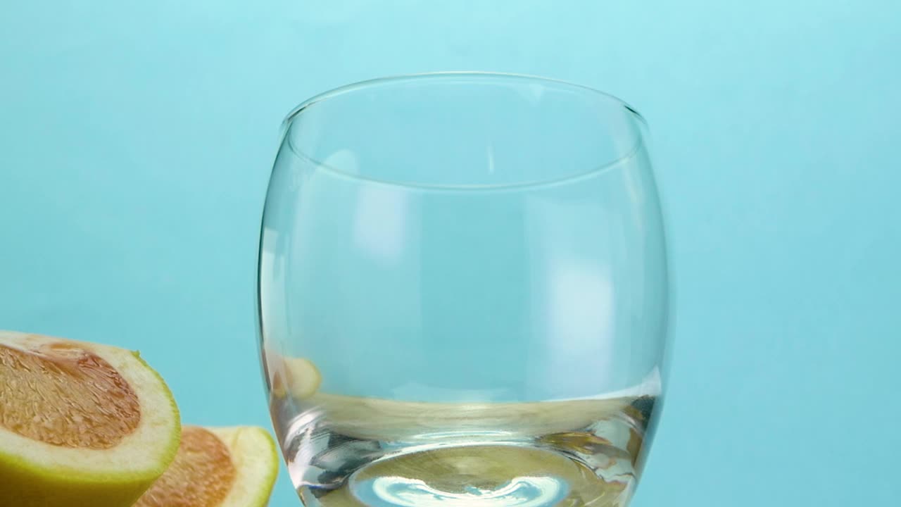 蓝底葡萄柚汁，酒精鸡尾酒加冰和水果。将西柚汁倒入玻璃杯中视频素材
