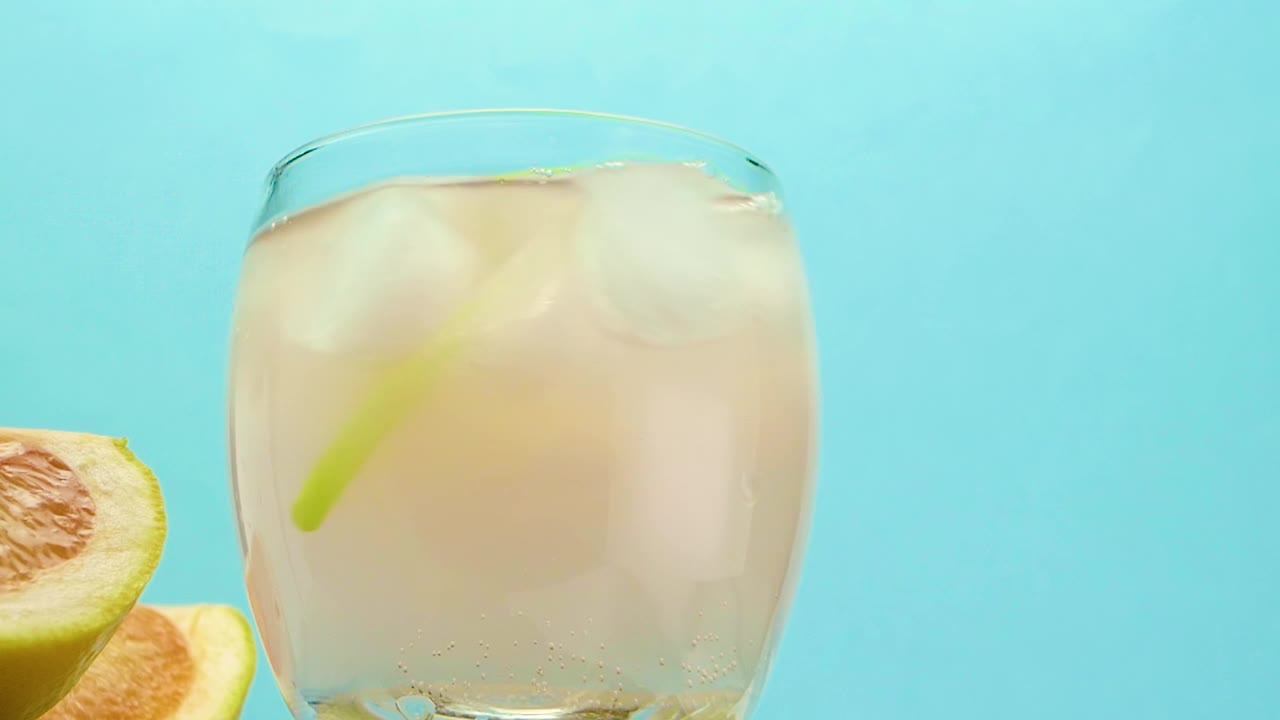 果汁和一管在一个玻璃杯和冰，葡萄柚鸡尾酒，酒精饮料在一个玻璃杯在实心木架子上的蓝色背景视频素材