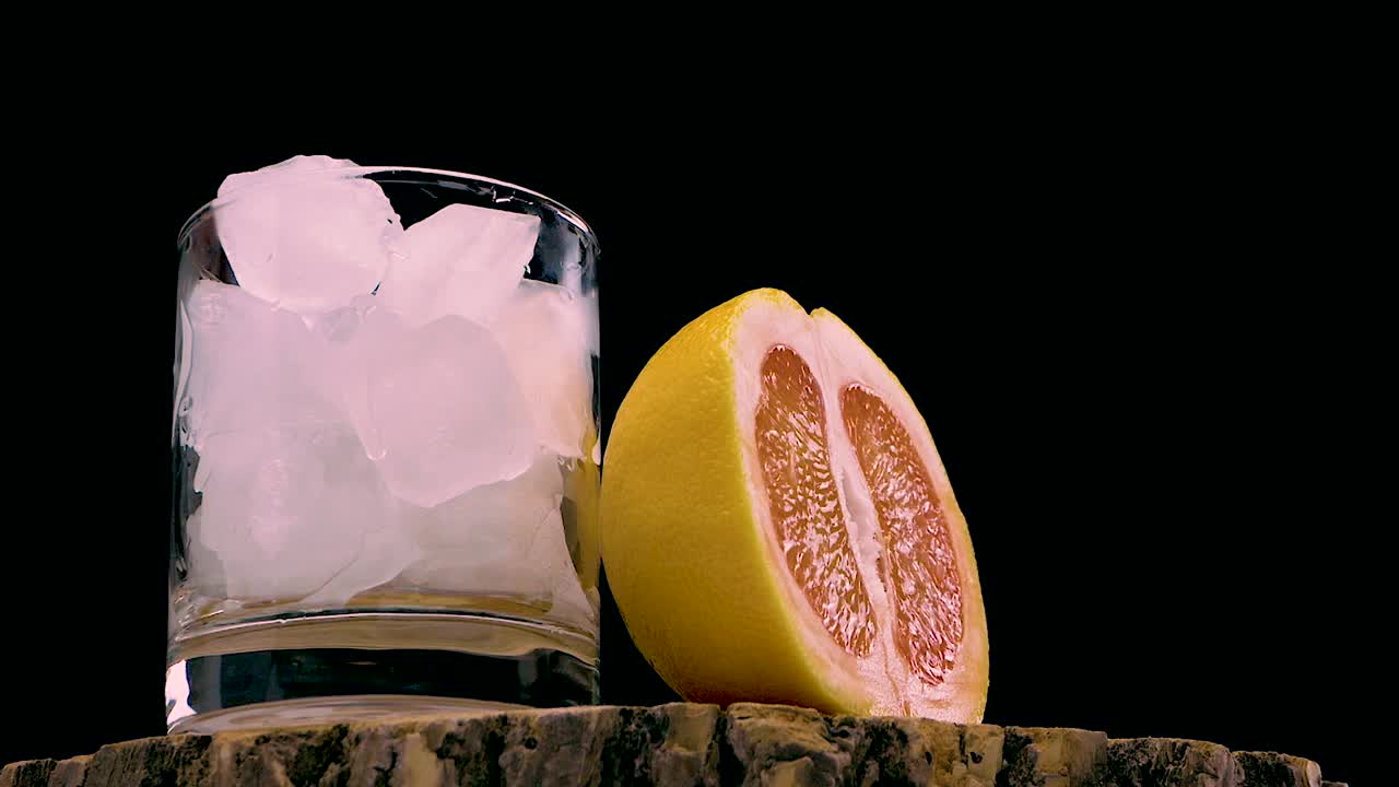 将西柚汁倒在黑色背景的木桌上。将冰镇的鸡尾酒与一片葡萄柚倒入杯中。天然果汁。夏天冰镇饮料视频素材