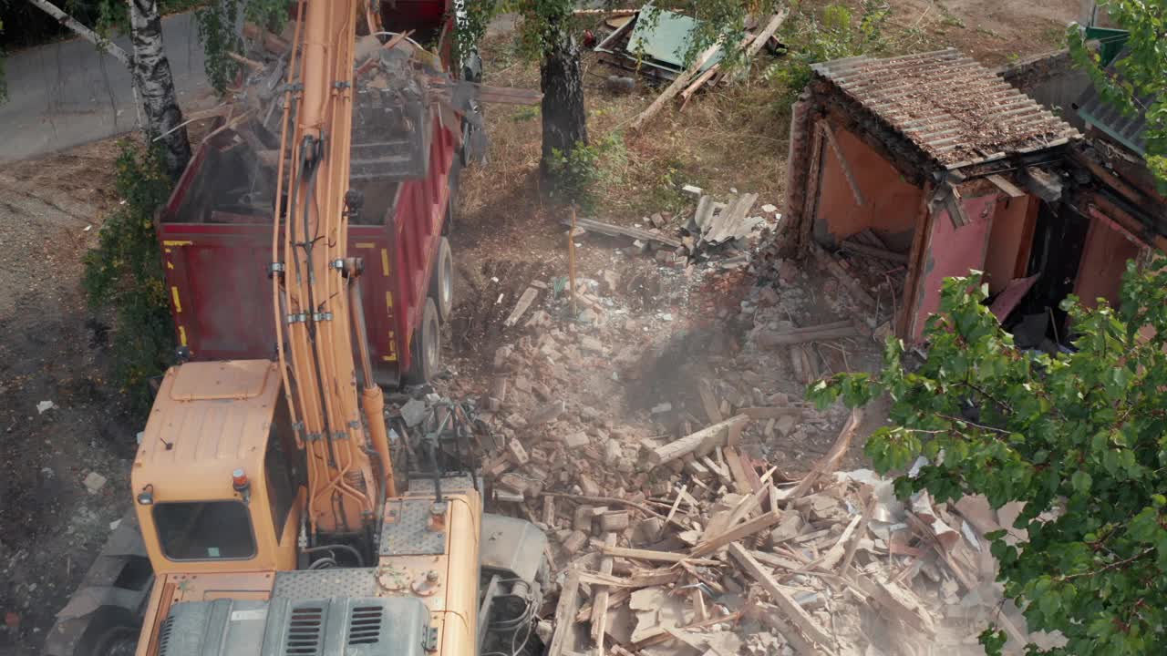为新建工程拆除房屋。挖掘机铲斗将垃圾装入卡车，鸟瞰图视频素材