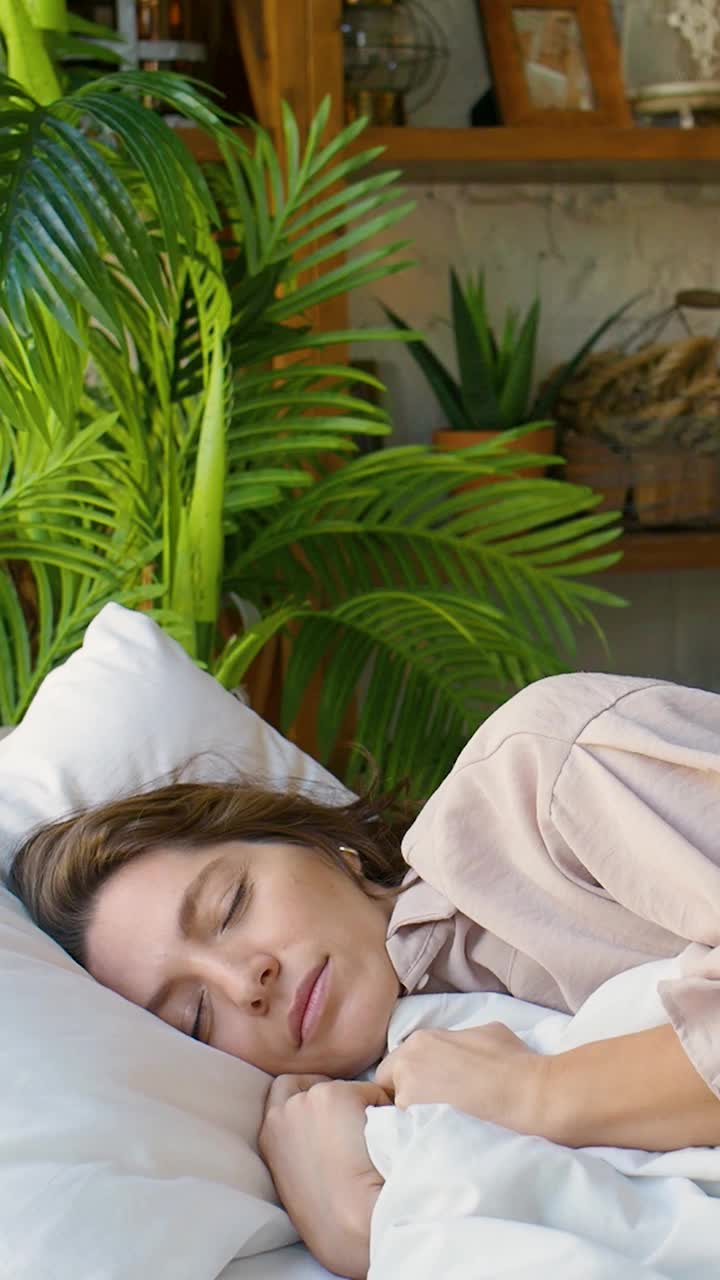 一段垂直视频显示，一名女子正在整理毛毯，在睡梦中微笑，甜美地睡着了视频素材