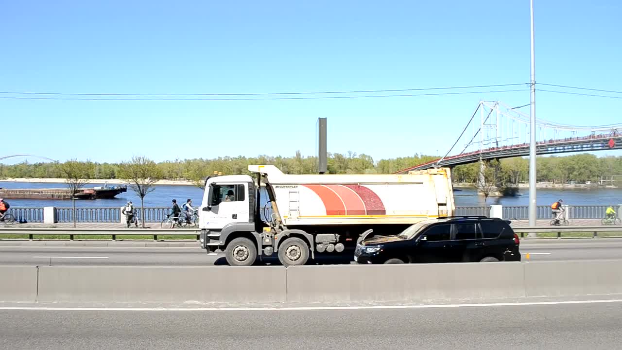 乌克兰基辅——2021年4月24日:汽车沿着路堤高速公路行驶。背景中，一艘货轮顺流而下。城市繁忙道路上的交通。视频下载