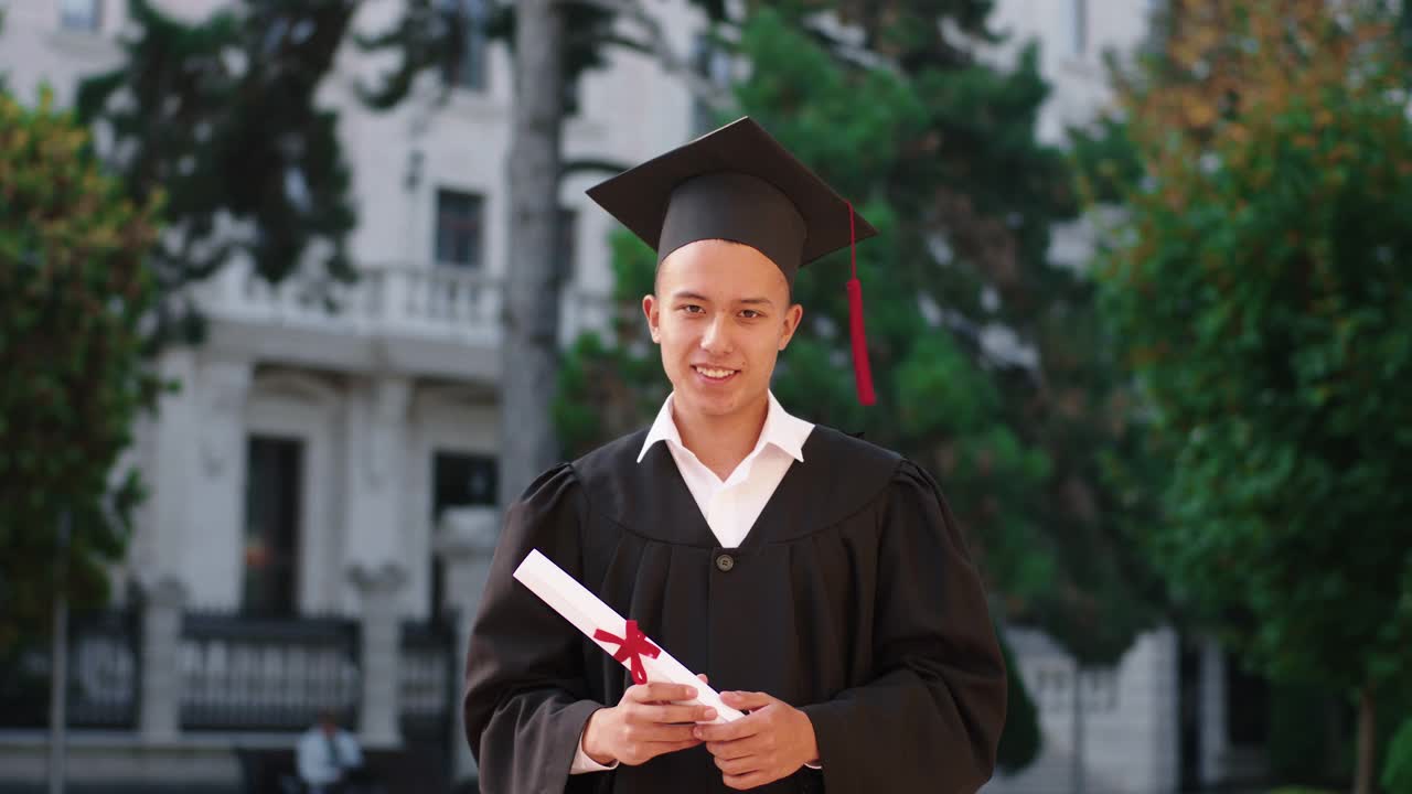 快乐有魅力的毕业生，拿着他的文凭，在相机前摆姿势，他戴着毕业帽视频素材