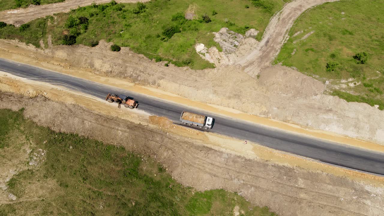 鸟瞰图重型矿用四轴自卸车为建设新铺路卸沙，推土机用两个铲斗倒着走视频素材