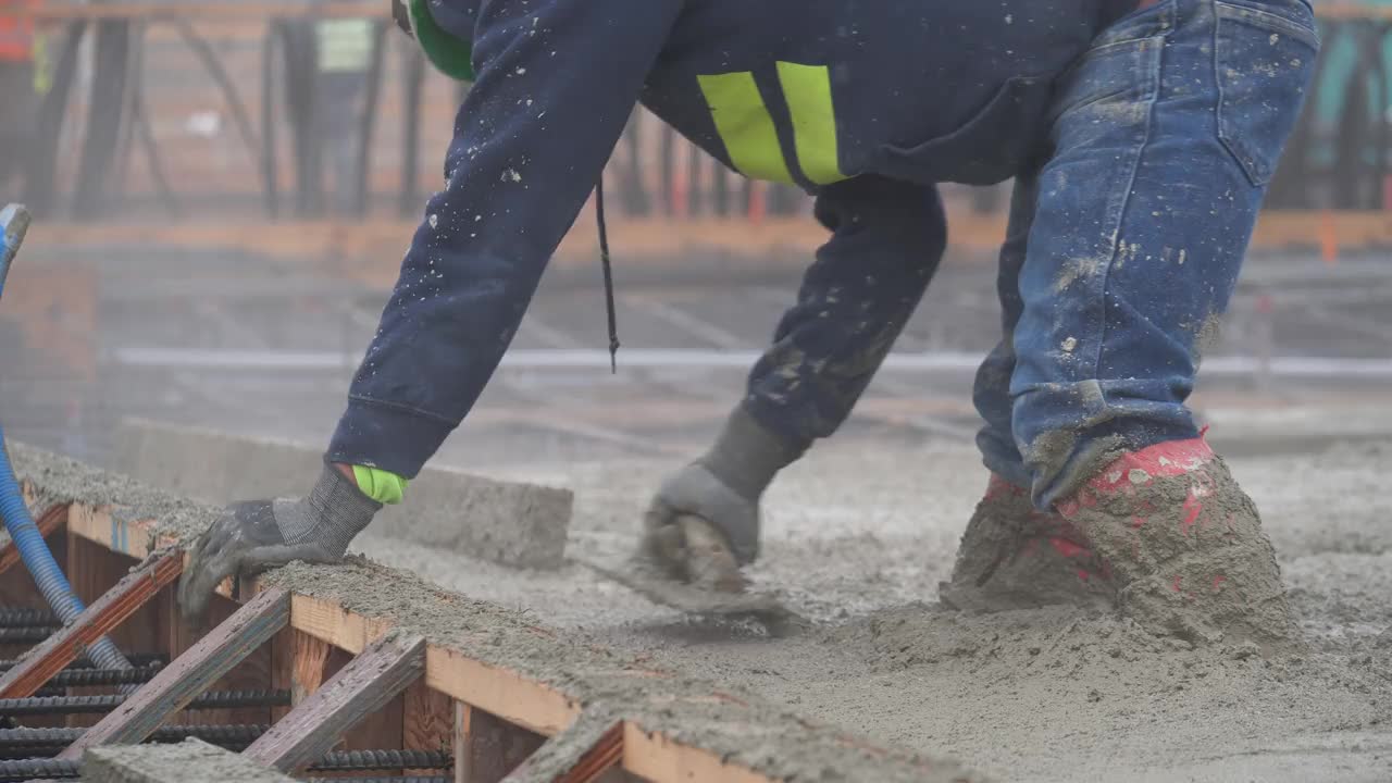 建筑工人使用手拖网完成一个大型混凝土浇注在一个商业工作地点。视频下载