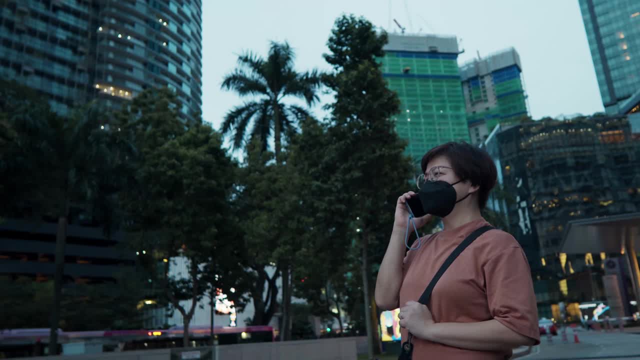 亚洲华人中间的成年女子晚上在霓虹灯下戴着口罩打电话视频素材