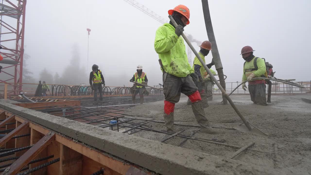 在一个大型商业工地，一队建筑工人正在用泵吊浇筑混凝土视频素材