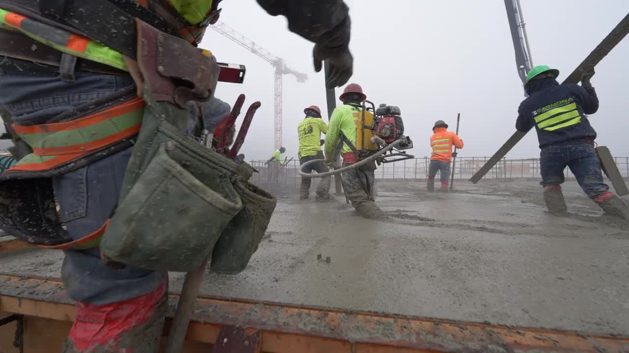 一组建筑工人在一个大型商业工地使用泵吊浇注混凝土。视频素材