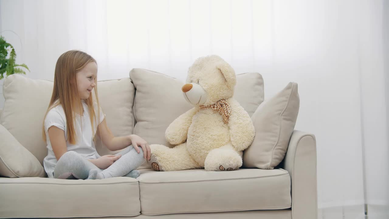 一个穿着白色衣服的金发小女孩在泰迪熊旁边的4k视频。视频素材