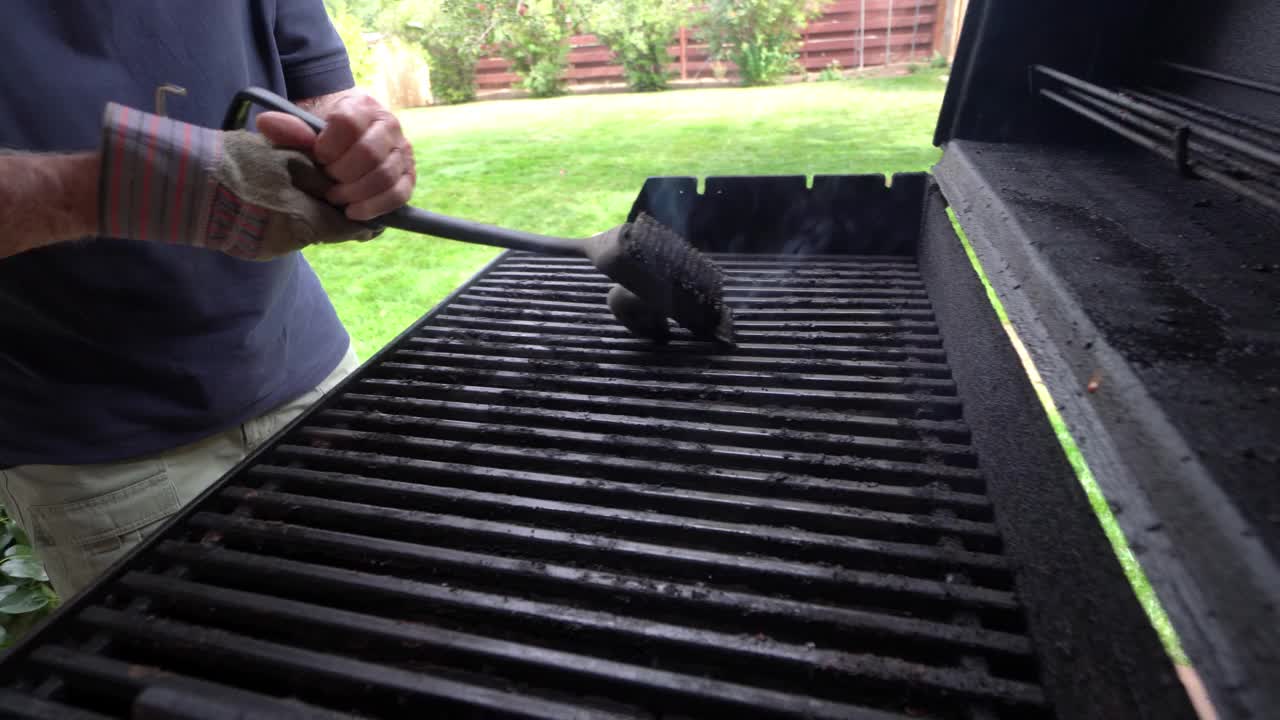一名白人男子站在户外后院刮烧烤架上烧焦的碎片视频下载