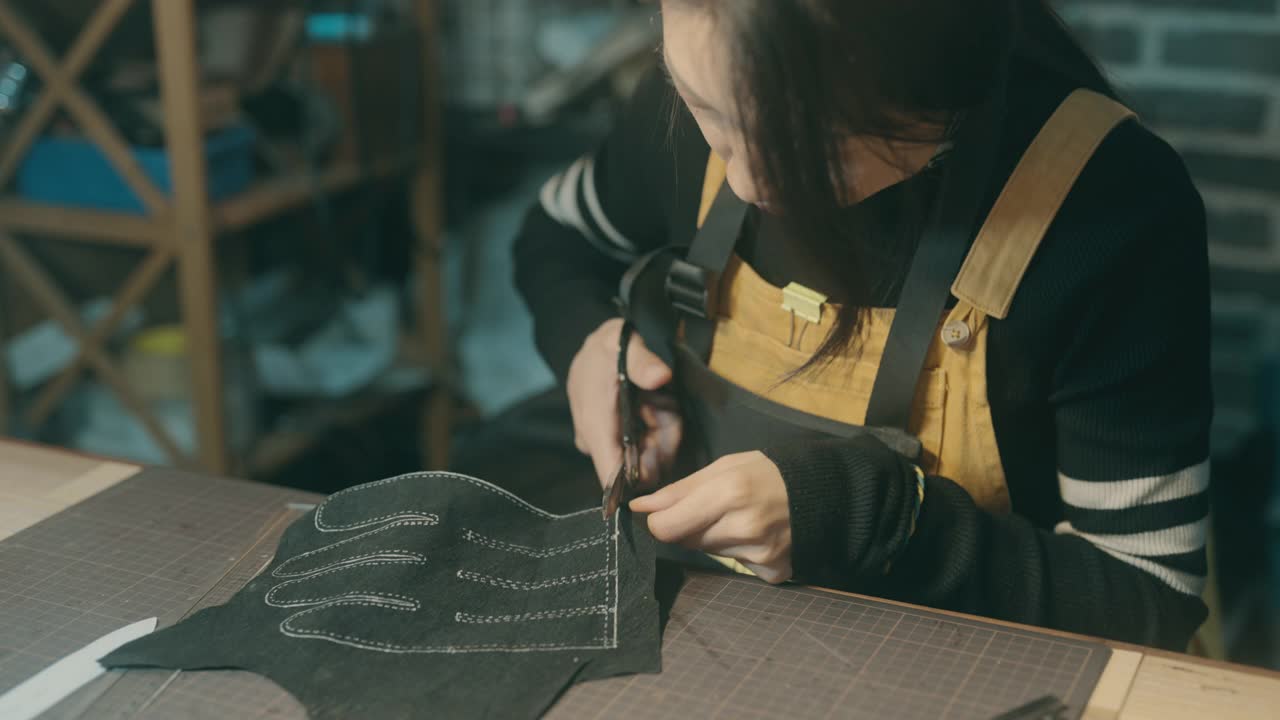 一位年轻的亚洲妇女正在工作台上做皮手套视频下载