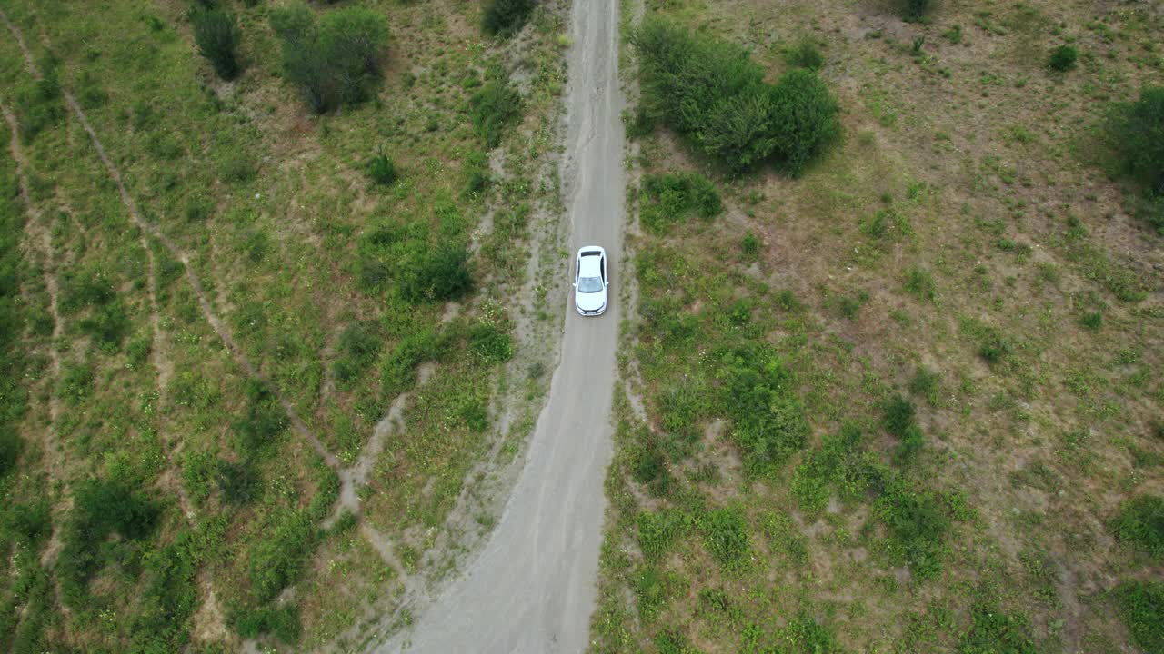 鸟瞰图的乘客白色汽车驾驶在农村狭窄的道路在山区。行动。车辆行驶在稀有的树木和绿色的山坡上视频素材