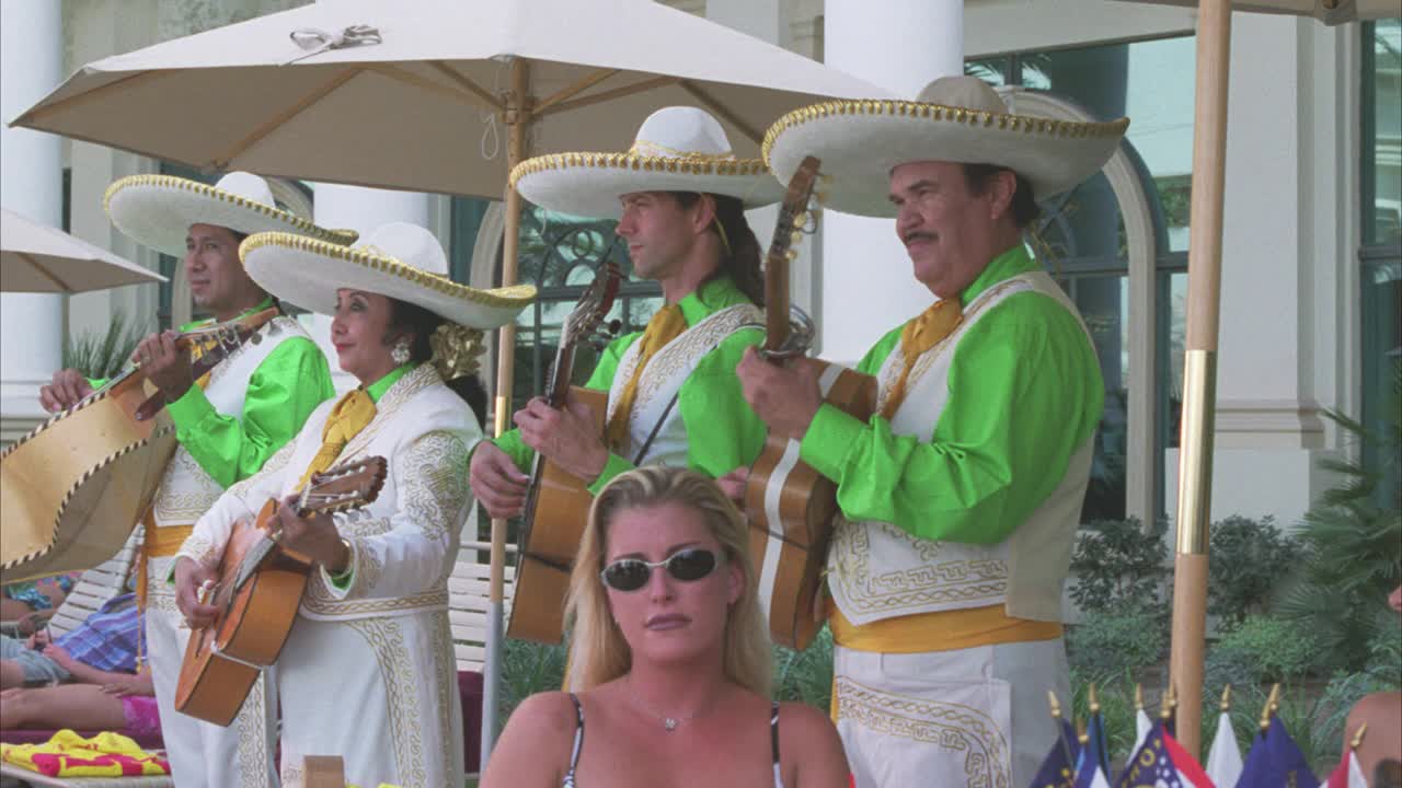 从右到左的乐手，可能是墨西哥流浪乐队，在泳池甲板上演奏。人们坐在桌子旁或懒洋洋地坐在椅子上。男男女女穿着泳衣跳舞。可能是热带假期或春假。视频素材