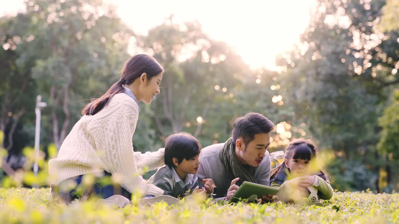 年轻的亚洲家庭在公园草地上放松视频下载