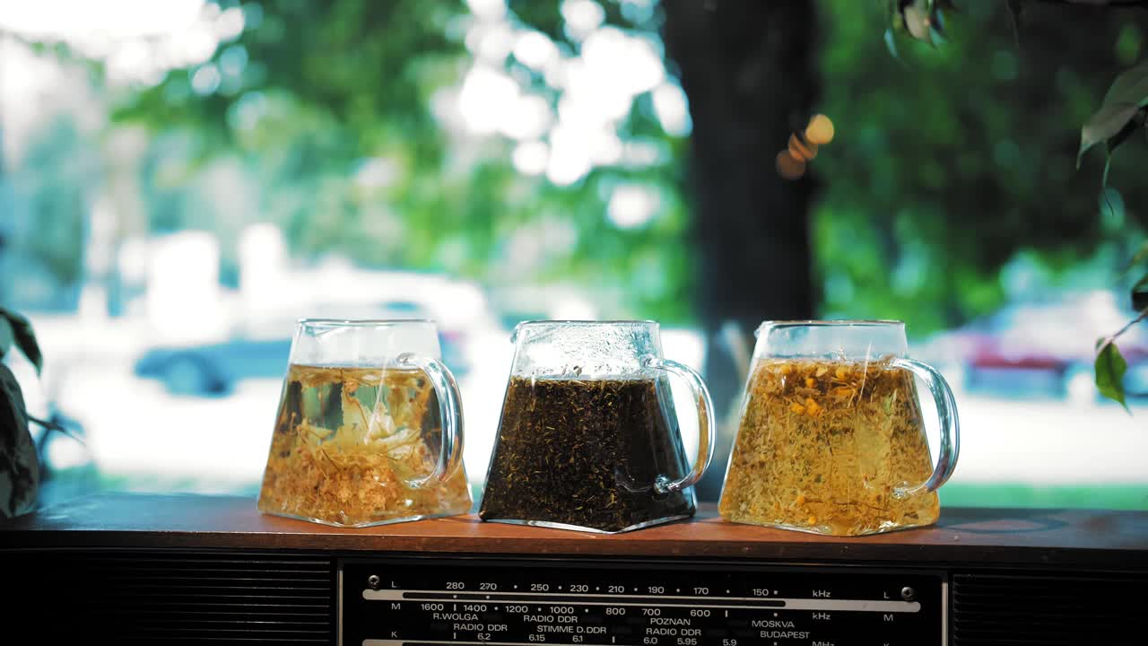 茶壶里的花草茶。茶饮料。特写镜头。三个玻璃茶壶，里面有不同的花草，五颜六色的茶。多叶花，碎薄荷，青柠，菩提树和甘菊茶视频素材