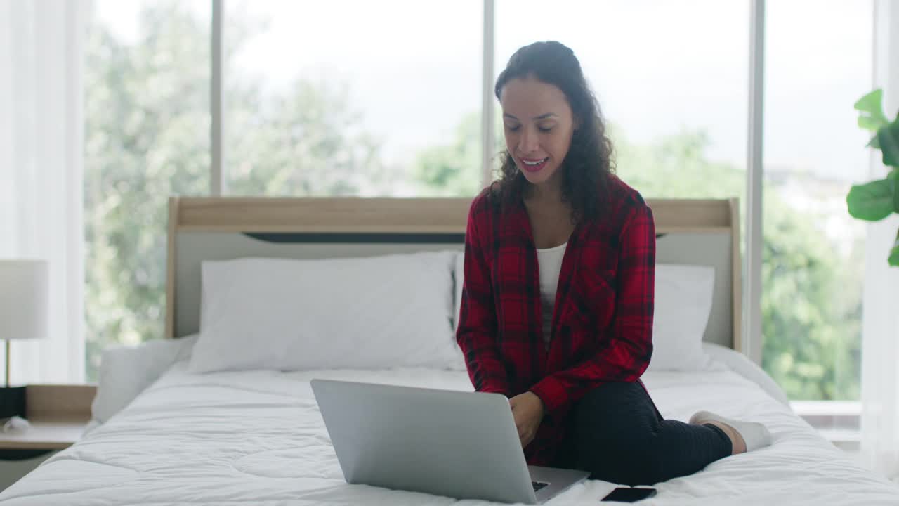 开朗的混血妇女在床上使用笔记本电脑视频素材