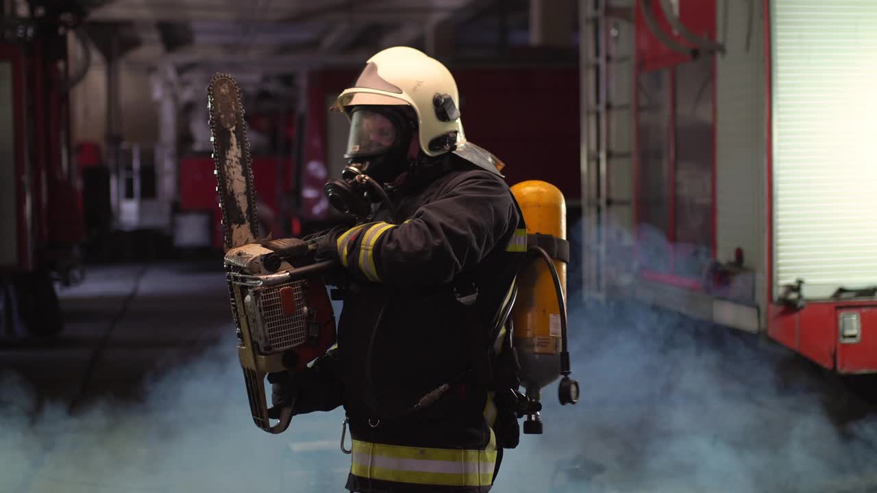 身穿全套装备、氧气面罩、电动液压切割工具的消防员肖像，背景是烟雾和消防车视频素材