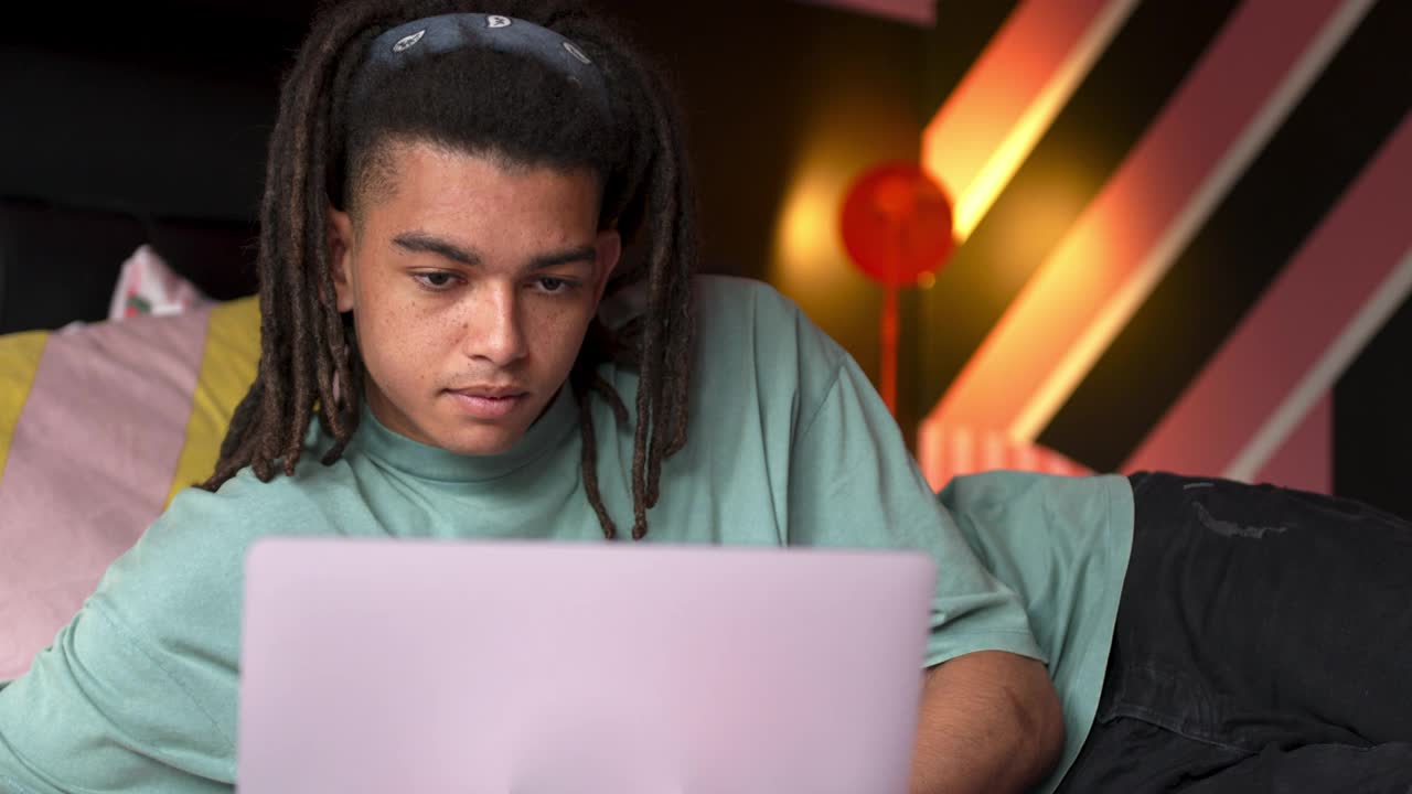 年轻的成年男学生在卧室里用笔记本电脑看着窗外思考视频下载